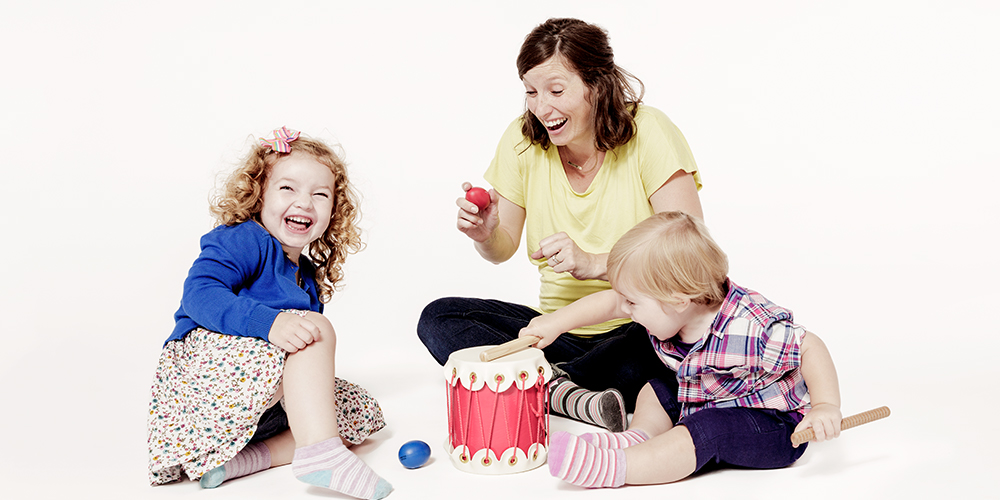 A mother happily playing with her son and daughter with balls and musical instrument